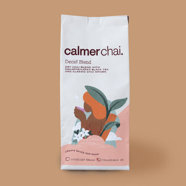 A tall white stand-up pouch of calmerchai Decaf Blend tea, featuring a minimalist illustration of a person meditating with orange and green leaves on a warm tan background.